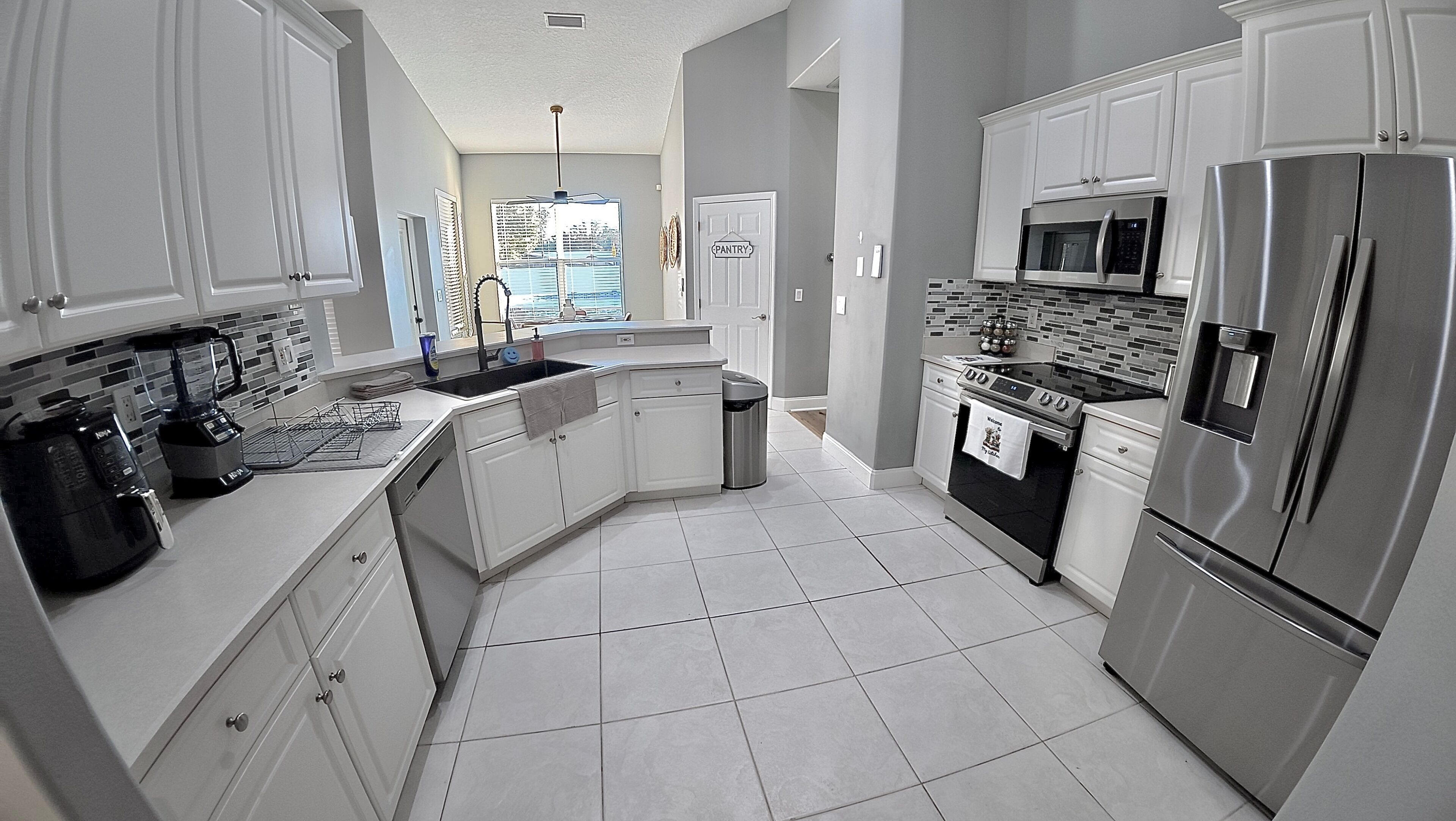 A modern kitchen with white cabinets, stainless steel appliances, and a tiled floor.