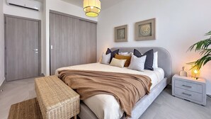 Une chambre moderne avec un lit, des tables de chevet, un luminaire suspendu et un climatiseur fixé au mur.
