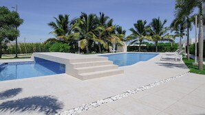 Une piscine avec des marches permettant d’y accéder, entourée de palmiers et sous un ciel dégagé.