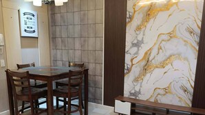 A dining area with a wooden table and chairs, a chandelier, a marble accent wall, and a bench. - The Gold Leaf Getaway: Stylish 1BR Urban Oasis (Taguig)
