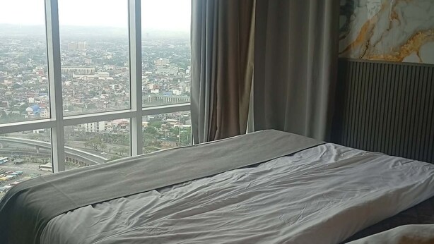 A bedroom with a large window, a bed, and a marble-patterned wall. - The Gold Leaf Getaway: Stylish 1BR Urban Oasis (Taguig)