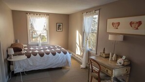 Ett sovrum med en säng, ett skrivbord, en stol, en lampa och en tavla på väggen.