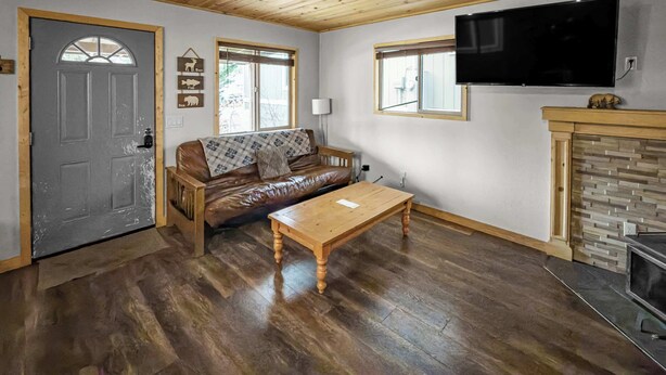Een gezellige woonkamer met een houten plafond, een leren bank, een houten salontafel, een aan de muur bevestigde televisie en een open haard.