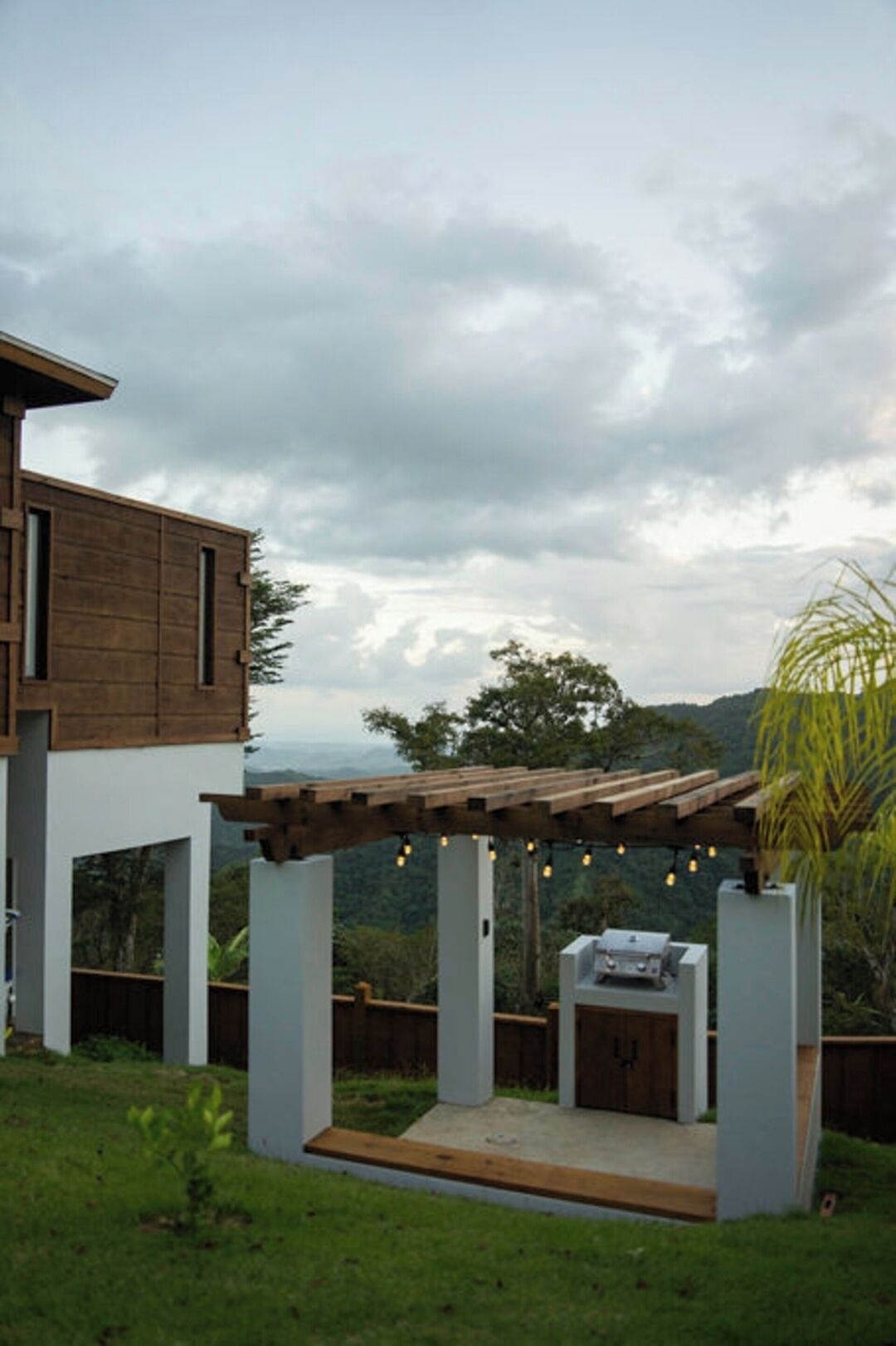 A modern outdoor patio with a pergola, a barbecue grill, and a view of a mountainous landscape.