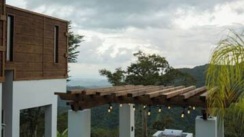 A modern outdoor patio with a pergola, a barbecue grill, and a view of a mountainous landscape.