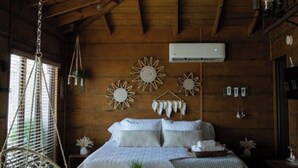 A cozy bedroom with a wooden ceiling, a bed with white linens, a hanging chair, and wall decor.