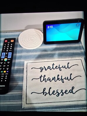 Un control remoto, una tableta y un posavasos bordado a mano con las palabras 'grateful', 'thankful' y 'blessed'.