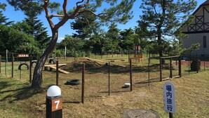 A fenced outdoor area with a wooden bench, a tree, and a sign with Japanese characters. - Heartland Hills in Noto 33 Umi no Wafu Zukuri (Nanao)