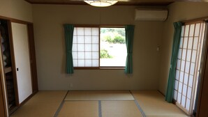 A traditional Japanese room with tatami flooring, a sliding door, and a window with curtains. - Heartland Hills in Noto 33 Umi no Wafu Zukuri (Nanao)