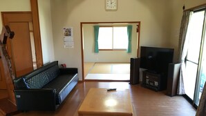 A living room with a sofa, a coffee table, a TV, and a tatami mat area. - Heartland Hills in Noto 33 Umi no Wafu Zukuri (Nanao)