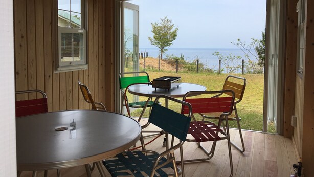 A wooden interior with a table and chairs, a window with a view of the sea, and a hanging light fixture. - Heartland Hills in Noto 33 Umi no Wafu Zukuri (Nanao)