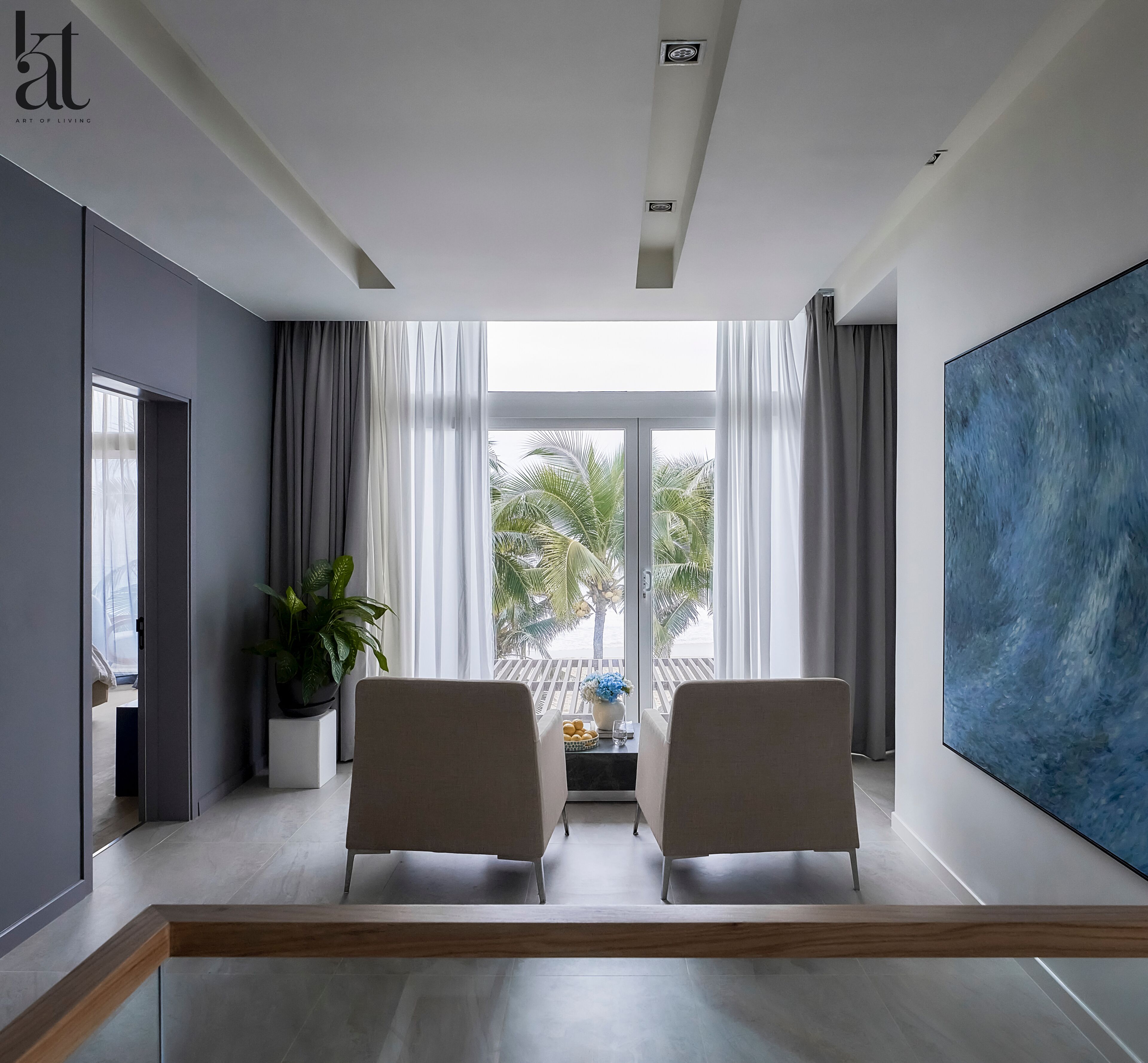 A modern living room with two armchairs, a large abstract painting, and a view of palm trees through the window.