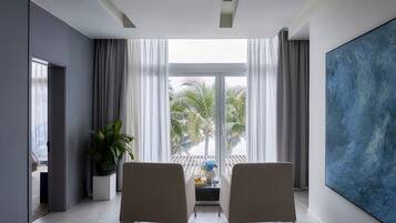 A modern living room with two armchairs, a large abstract painting, and a view of palm trees through the window.