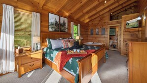 Ein Schlafzimmer einer Holzhütte mit einem Bett, Nachttischen, einem Schminktisch und einem Fernseher.