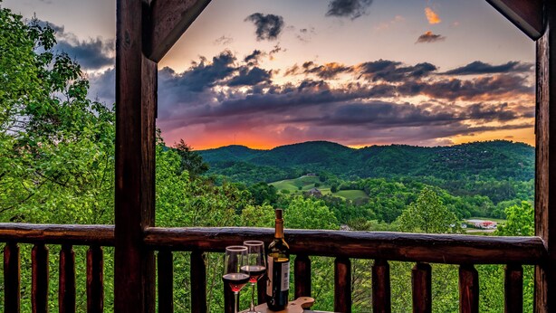 Ein Holzbalkon mit Panoramablick über ein üppiges Tal und einen Sonnenuntergang.
