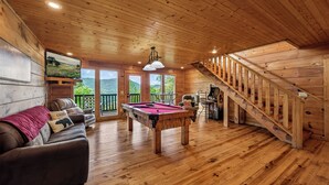 Ein Holzinnenraum mit Poolbillard, Sofa und Treppe.