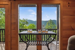 A wooden deck with a table and chairs, a view of green hills, and a clear sky. - The Overlook - Hot Tub, Game Room, Mountain Views! (Sevierville)