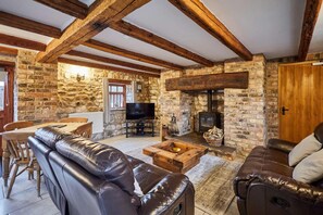 A cozy living room with stone walls, wooden beams, leather sofas, a TV, and a fireplace. - Host Stay Mill House Brid (Bridlington)