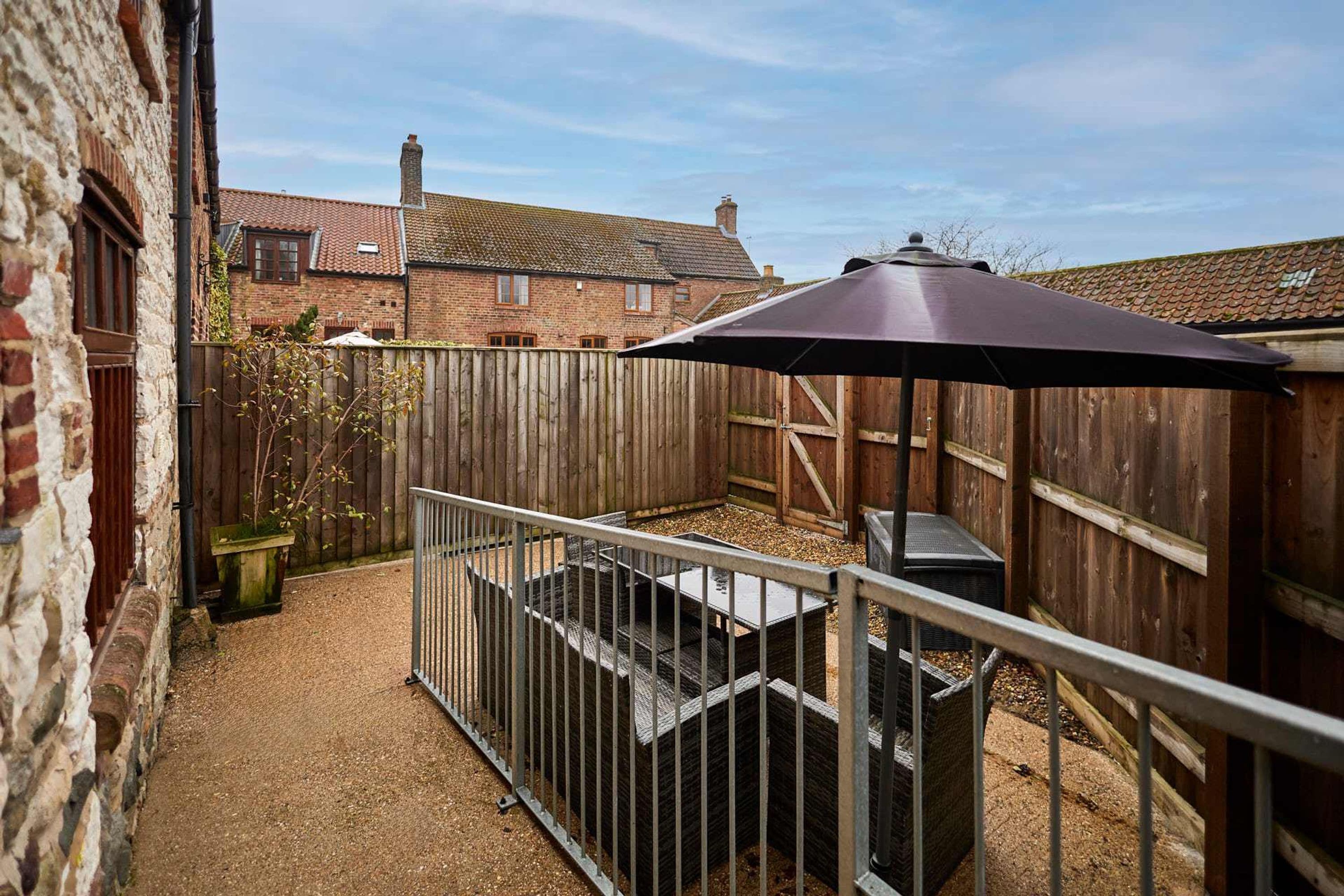 A fenced backyard with a patio area, a wooden fence, and a brick building in the background.