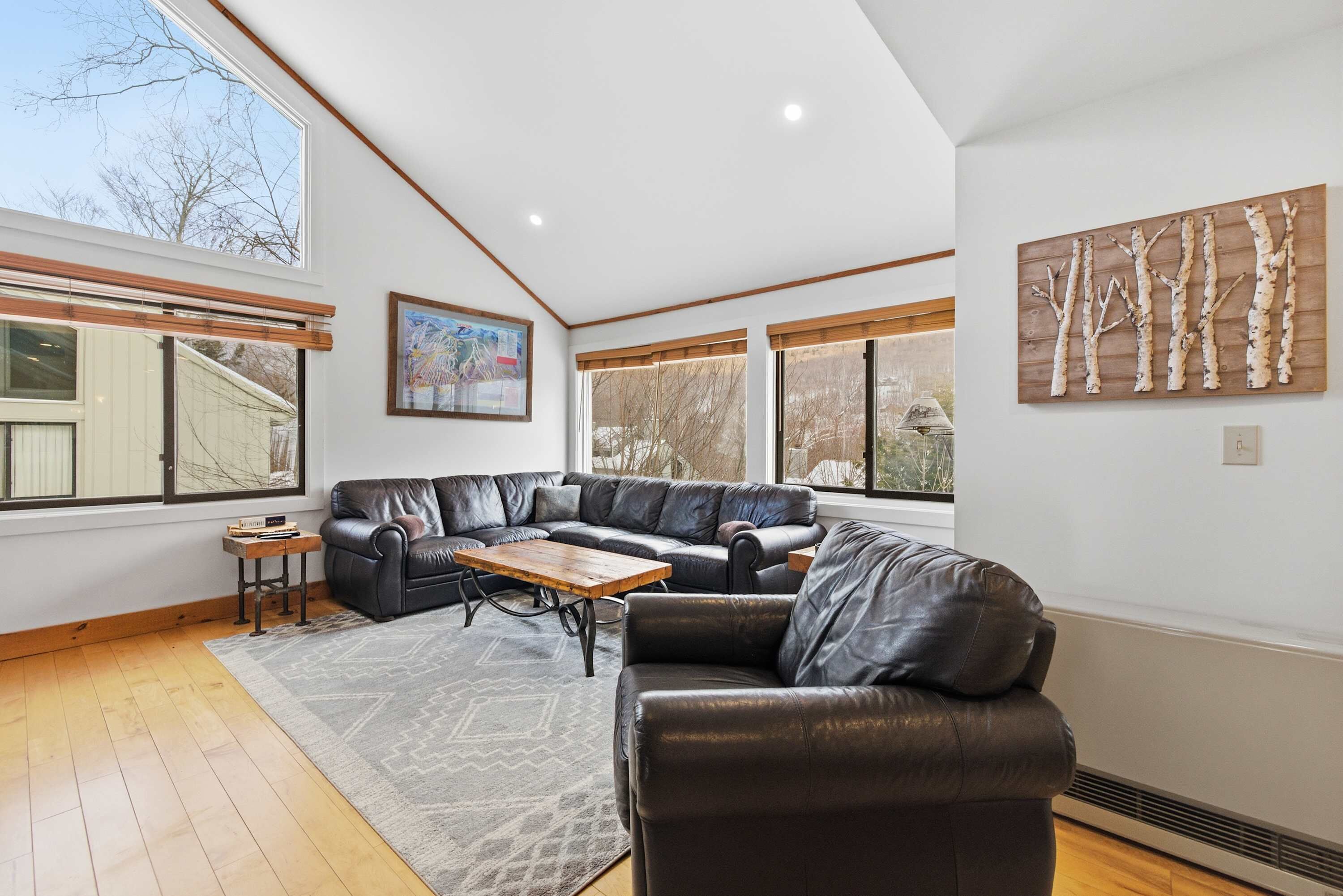 Un salon moderne avec un canapé d’angle, une table basse en bois et de grandes fenêtres qui laissent entrer la lumière naturelle.