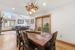 Ein Essbereich mit einem Holztisch und Stühlen, einer Chandelierleuchtre und Blick ins Freie durch eine Schiebetür.