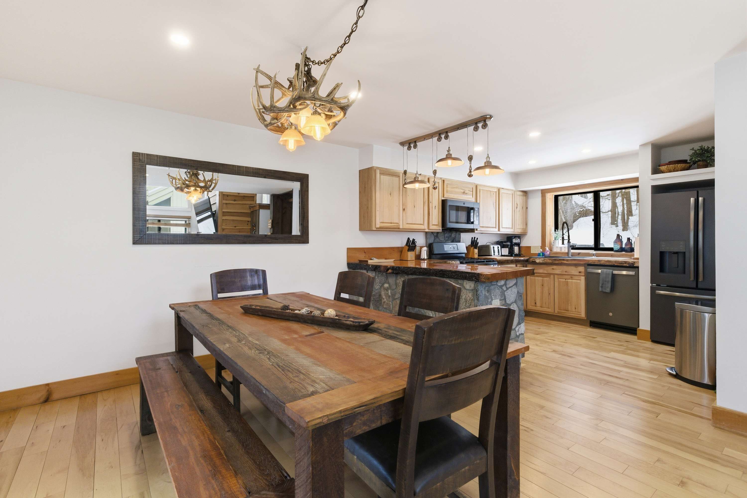 A modern kitchen with wooden cabinets, a central island, and a dining area with a wooden table and benches.