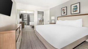 A hotel room with a large bed, a wooden dresser, a flat-screen TV, and two framed artworks on the wall.