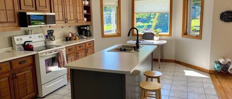 A kitchen with wooden cabinets, a large island, a microwave, a stove, and a sink.
