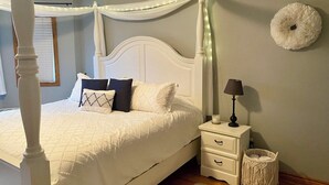 Un dormitorio con una cama con dosel, una mesita de noche con lámpara y un tapiz decorativo.