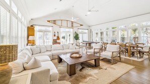 Uma sala de estar ampla, com um sofá seccional grande, uma mesa de centro de madeira e uma área de jantar com cadeiras e mesa de madeira.