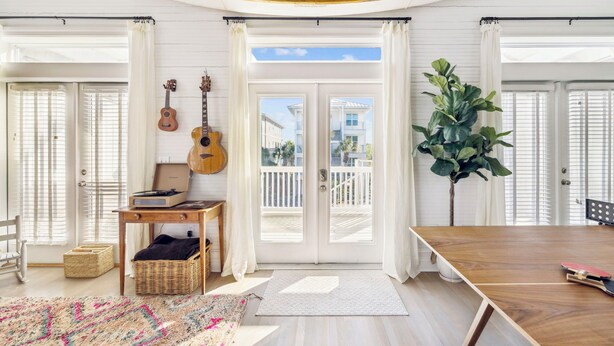 Um quarto espaçoso com uma grande mesa de madeira, um violão e um vaso com planta.