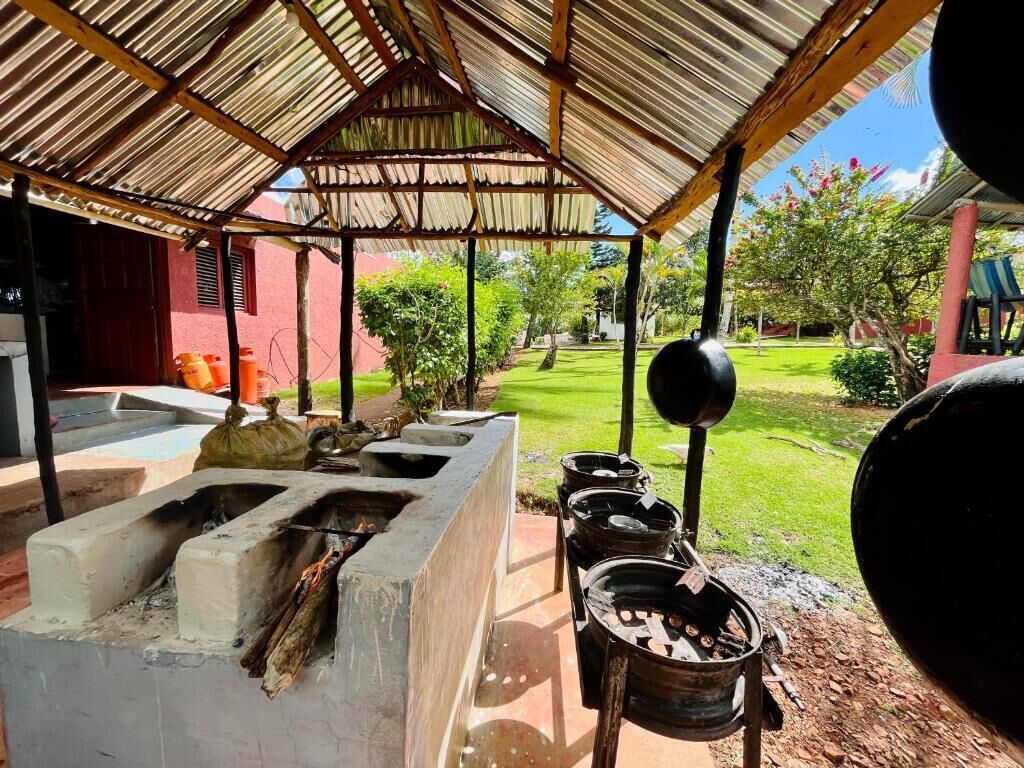 Una zona de cocina al aire libre con una parrilla y ollas, una estructura de concreto y un techo de paja.