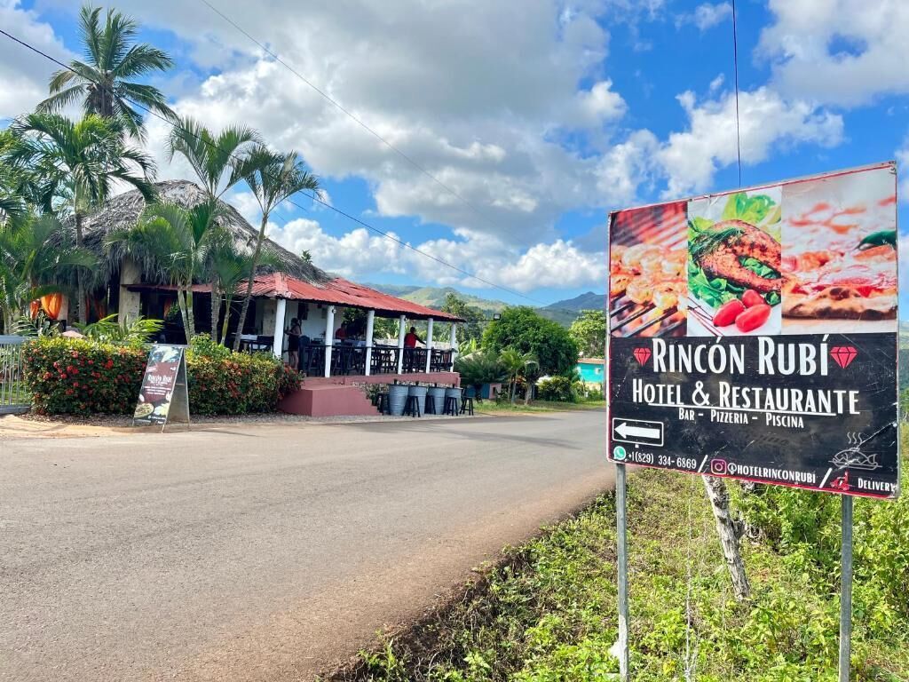 Un cartel para el Hotel & Restaurante Rincon Ruby, mostrando el edificio y el paisaje tropical circundante.