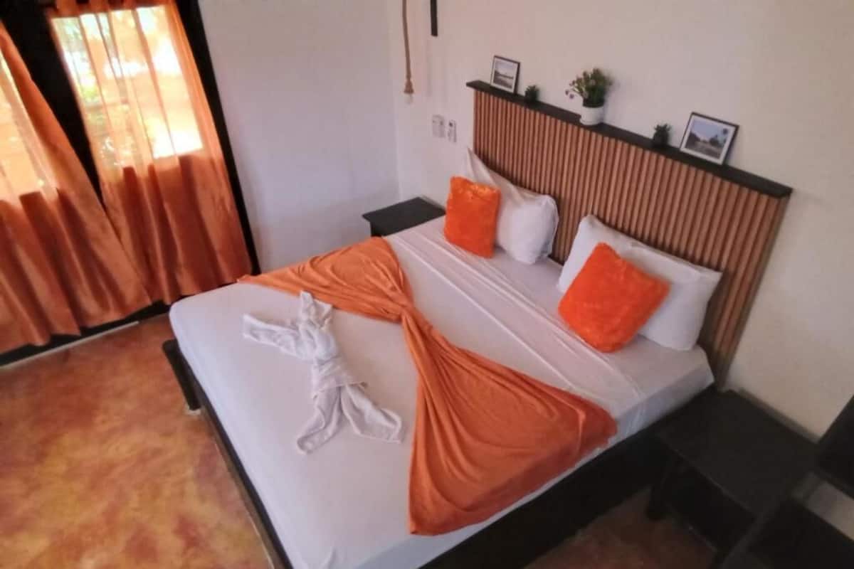 A neatly made bed with orange and white bedding, a wooden headboard, and a small bedside table with a lamp.