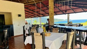 Een terras met tafels en stoelen, een bar en uitzicht op de oceaan.