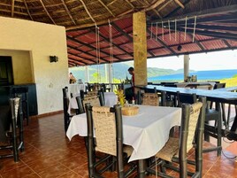 Un área de comedor al aire libre con mesas y sillas, zona de bar y vista al océano.