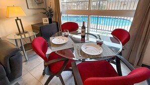 Een eetruimte met een glazen tafel, rode stoelen en uitzicht op een zwembad.