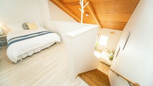 A bedroom with a wooden ceiling, a bed with a white and blue bedspread, and a staircase leading to another room. - Miraie Yokkaichi Hinaganishi (Yokkaichi)