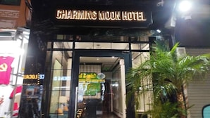 The exterior of the Charming Moon Hotel with a neon sign, glass entrance, and a palm tree in the foreground. - Charming Moon Hotel (Hanoi)