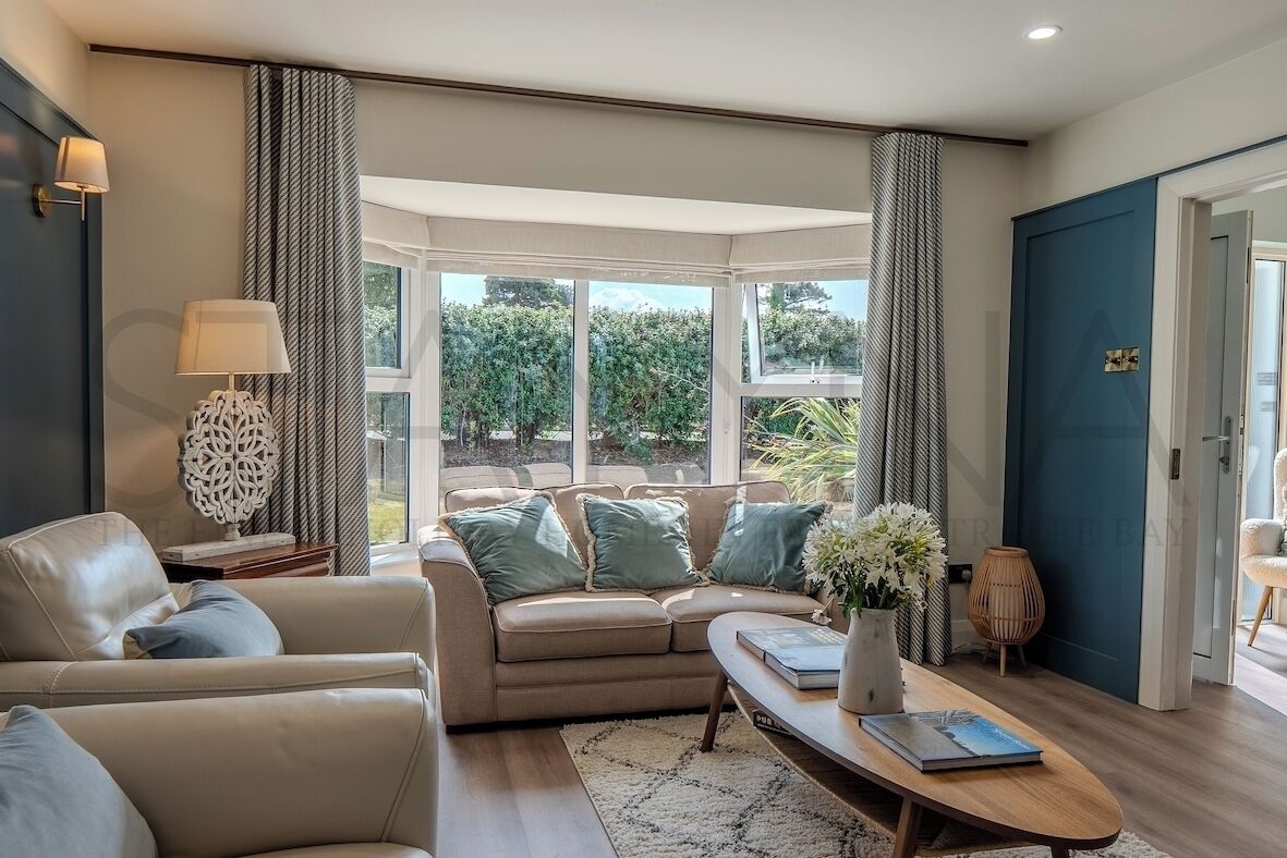 A modern living room with a sofa, coffee table, and a view through large windows.