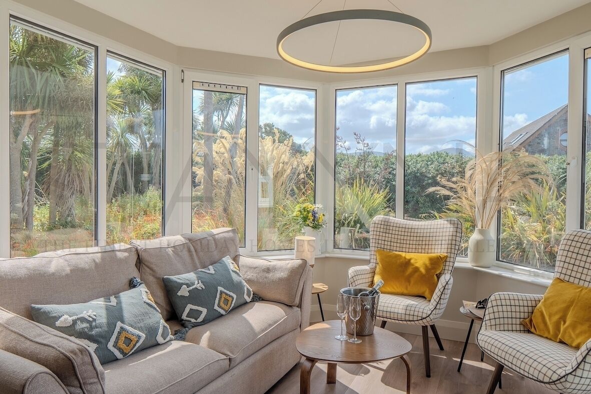 A modern living room with a sofa, armchairs, and a coffee table, large windows offering a view of tropical vegetation.