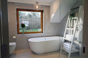 Une salle de bain moderne avec une baignoire sur pieds, une fenêtre donnant sur la verdure et une cabine de douche en verre.