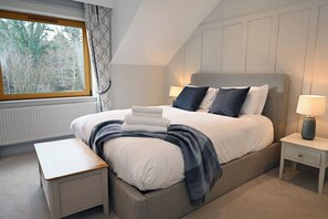 Une chambre à coucher avec un grand lit, des tables de chevet, un banc et une fenêtre avec des rideaux.