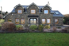 Une maison en pierre à la façade symétrique, dotée de nombreuses fenêtres et d’un jardin bien entretenu.