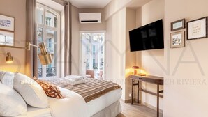 Hotellihuone, jossa on sänky, yöpöytävalaisimet, taulutelevisio ja ikkuna, josta on näkymä rakennuksiin.