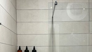 A shower area with a glass door and a shelf holding three bottles. - Noon Properties 1 Beachside 1BR in Dh rmi (Himarë)