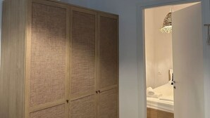 A room with a large wooden wardrobe, a door leading to a bathroom, and a hanging light fixture. - Noon Properties 1 Beachside 1BR in Dh rmi (Himarë)