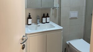 Un baño con un lavamanos blanco, dos botellas de jabón líquido, un espejo sobre el lavamanos y un inodoro.
