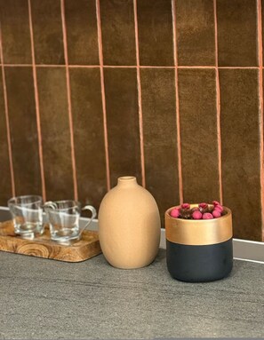 Een beige vaas en een zwarte en gouden container met roze bloemen op een houten dienblad.