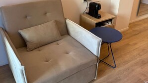 Un sofá color beige con un cojín, una mesita con cafetera y un espejo en la pared.